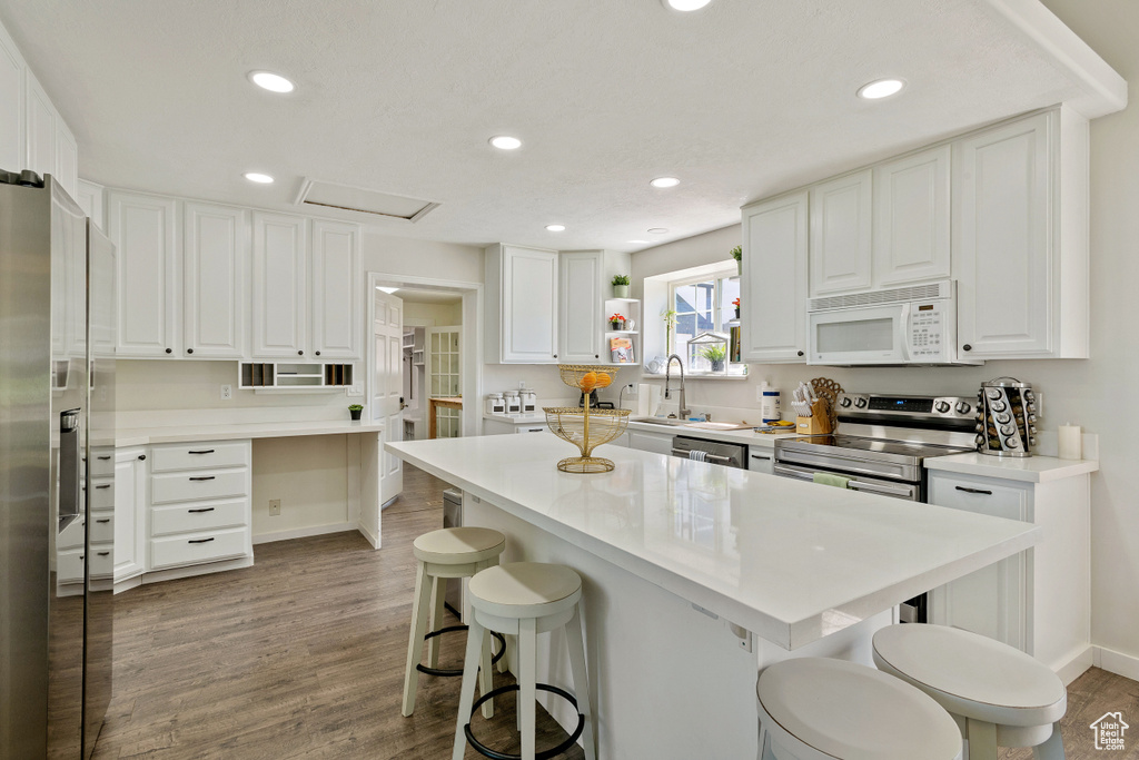 Kitchen featuring open shelves, stainless steel appliances, a breakfast bar area, and white cabinetry