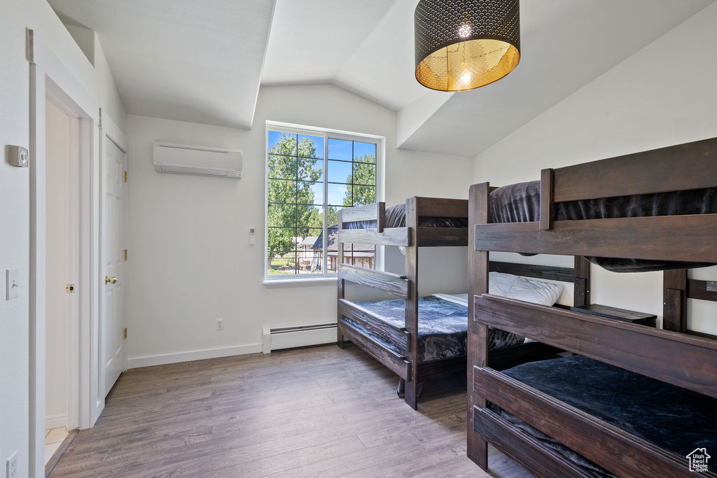 Bedroom with baseboard heating, wood finished floors, baseboards, an AC wall unit, and lofted ceiling