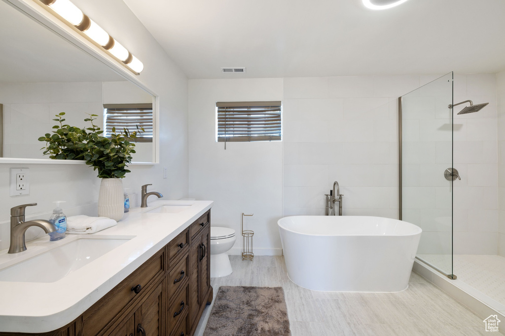 Bathroom with double vanity, a soaking tub, tiled shower, and toilet