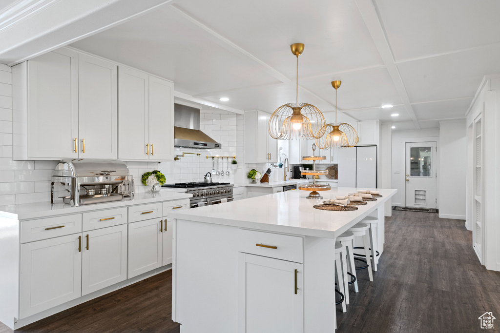 Kitchen with decorative backsplash, white cabinetry, and wall chimney range hood