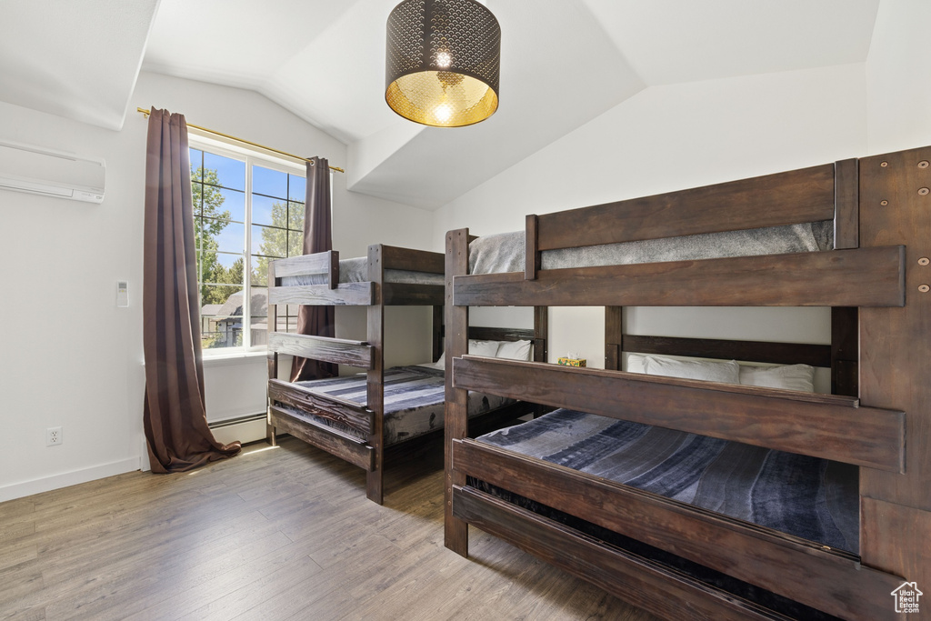 Bedroom featuring vaulted ceiling, wood finished floors, baseboard heating, an AC wall unit, and baseboards