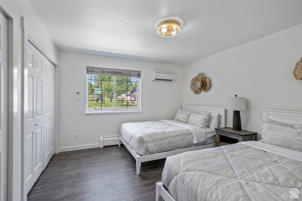 Bedroom with dark wood-style flooring, baseboards, a baseboard radiator, a closet, and an AC wall unit