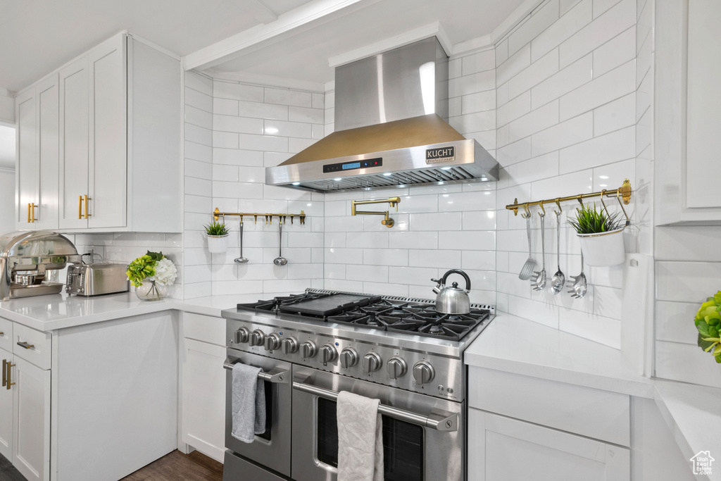 Kitchen featuring backsplash, range with two ovens, light countertops, white cabinets, and wall chimney exhaust hood