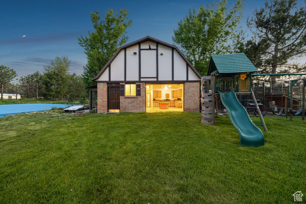 Back of property at dusk with a playground, a yard, brick siding, and an outbuilding