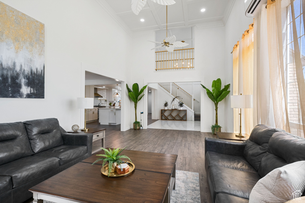 Living room with wood finished floors, a towering ceiling, ornamental molding, stairway, and coffered ceiling