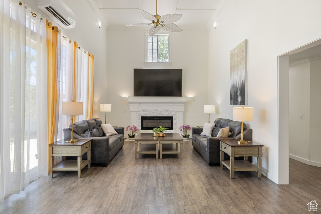 Living area featuring a wall unit AC, a towering ceiling, crown molding, wood finished floors, and a ceiling fan