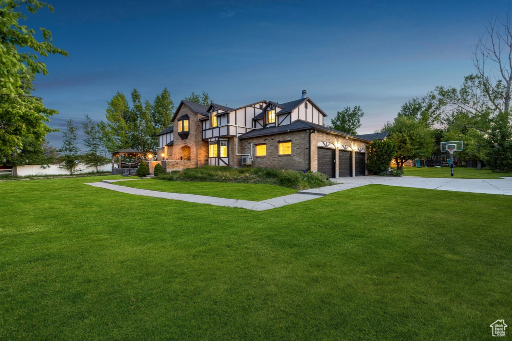 Tudor house with a front yard, brick siding, a garage, and driveway