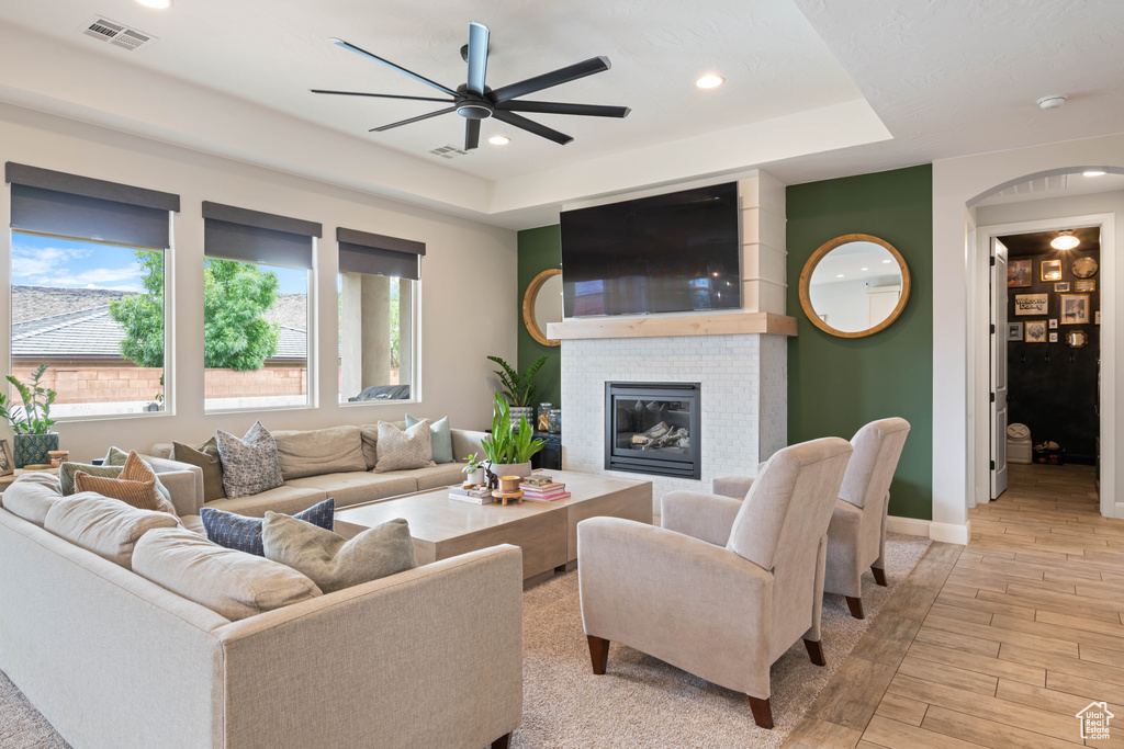 Living room with a ceiling fan, light wood finished floors, baseboards, a fireplace, and arched walkways