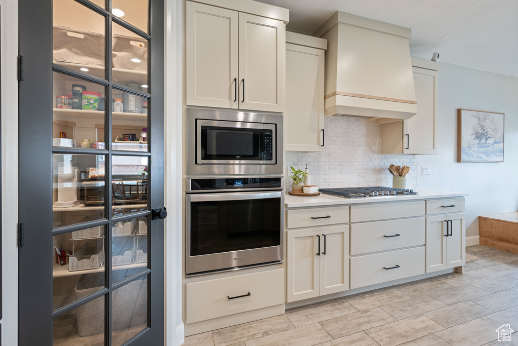 Kitchen with built in appliances, custom exhaust hood, tasteful backsplash, light countertops, and white cabinetry