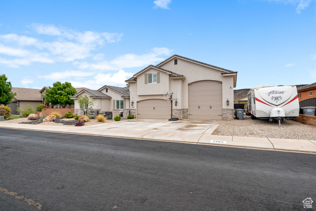 View of front of home with stucco siding, stone siding, driveway, and a garage