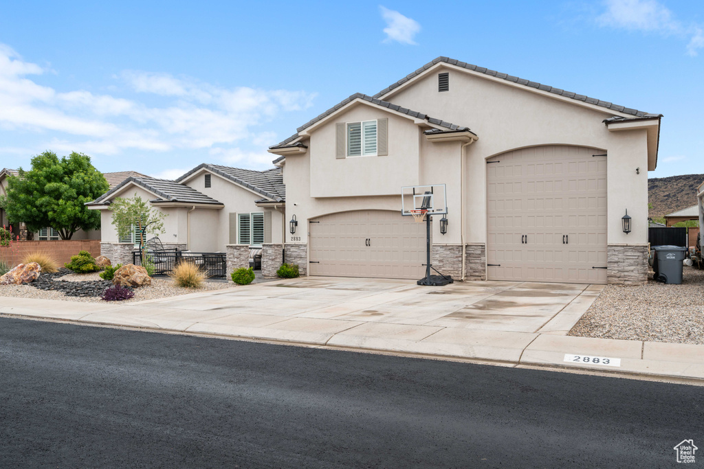View of front of home with stone siding, fence, stucco siding, and driveway