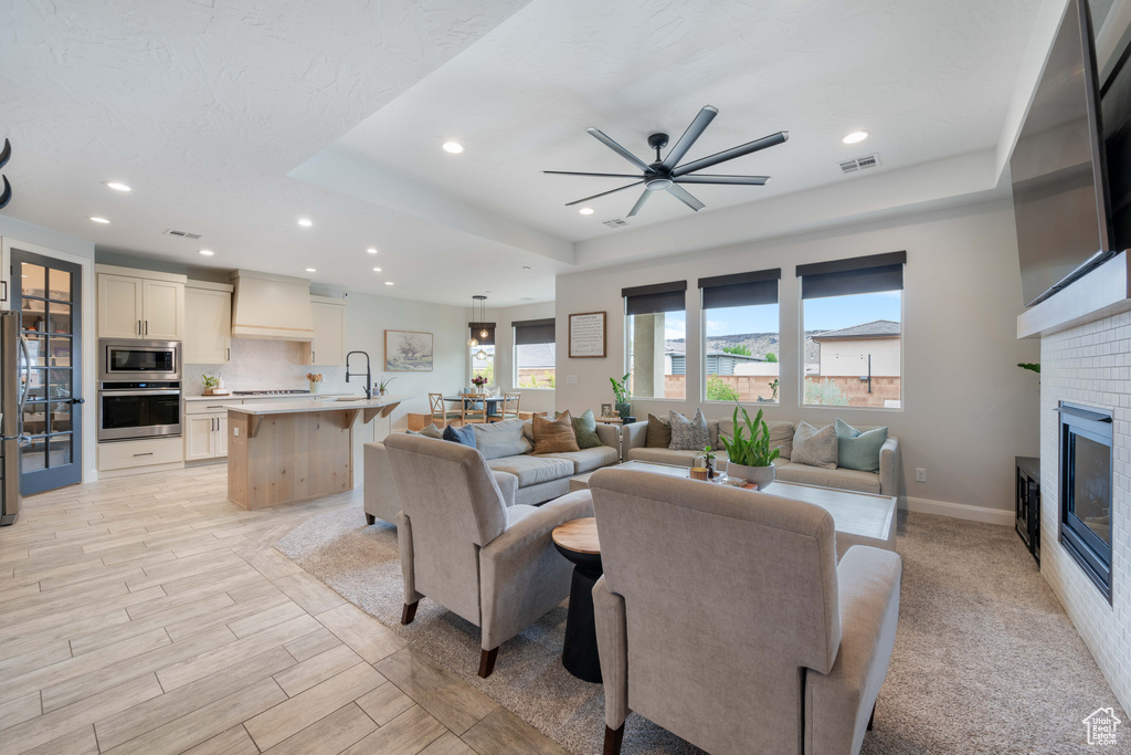 Living area with recessed lighting, a ceiling fan, a glass covered fireplace, baseboards, and a tray ceiling