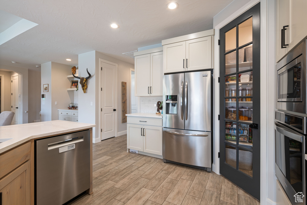 Kitchen with appliances with stainless steel finishes, light countertops, light wood-style floors, backsplash, and recessed lighting