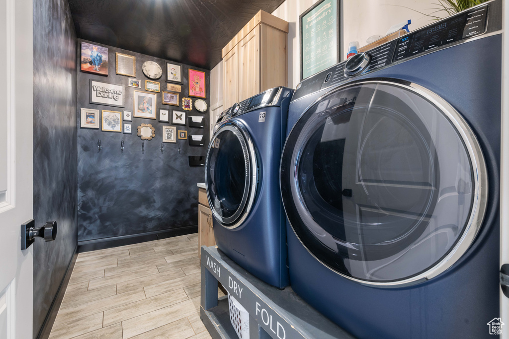 Laundry room featuring washer and clothes dryer, light wood-style flooring, and cabinet space