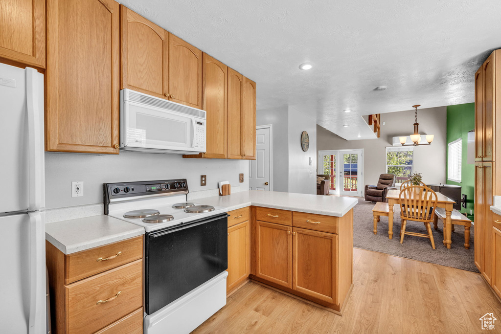 Kitchen with white appliances, a peninsula, light wood-style floors, light countertops, and open floor plan