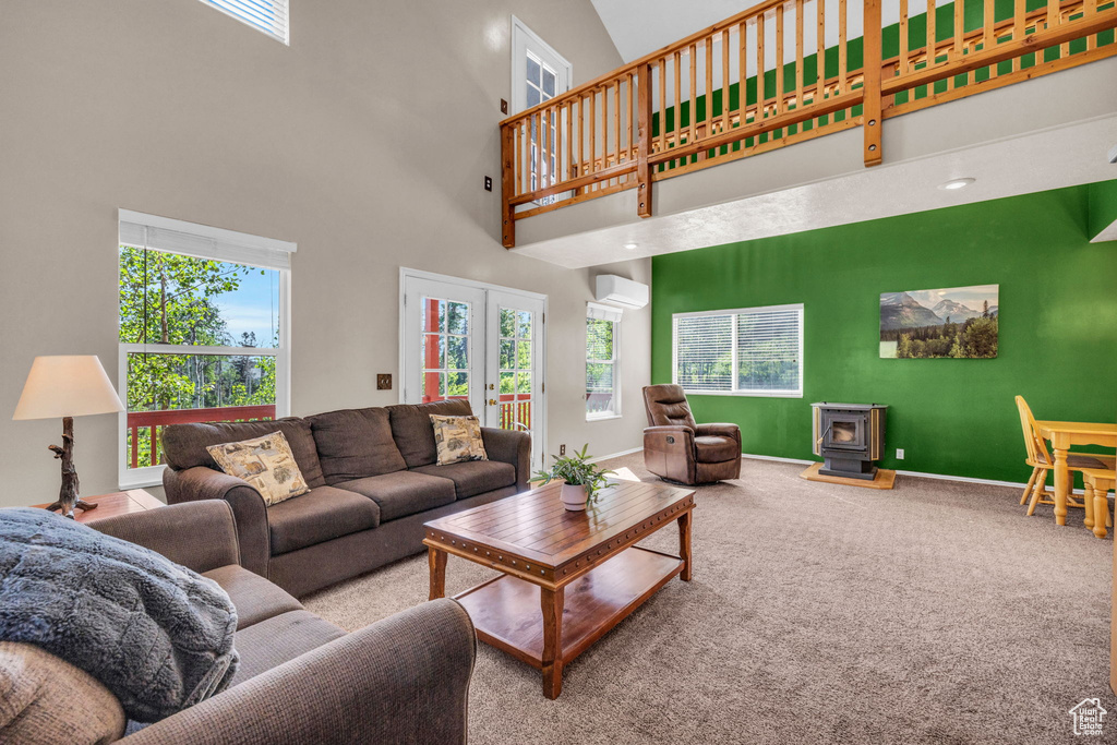 Living area with a wood stove, carpet, a wall mounted air conditioner, baseboards, and a high ceiling