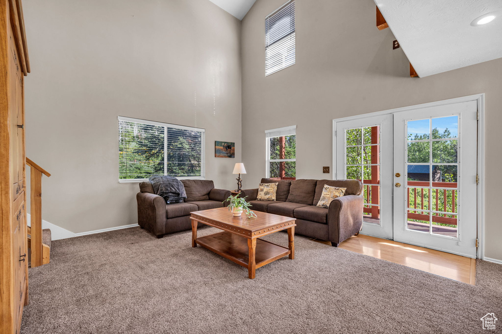 Carpeted living room with high vaulted ceiling, french doors, baseboards, and stairway