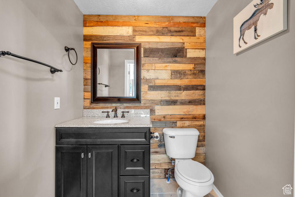 Half bath with wooden walls, toilet, and vanity