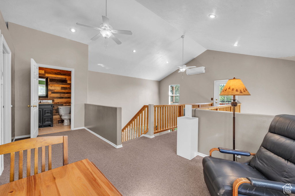 Living area featuring an upstairs landing, a ceiling fan, a wall unit AC, a wood stove, and lofted ceiling