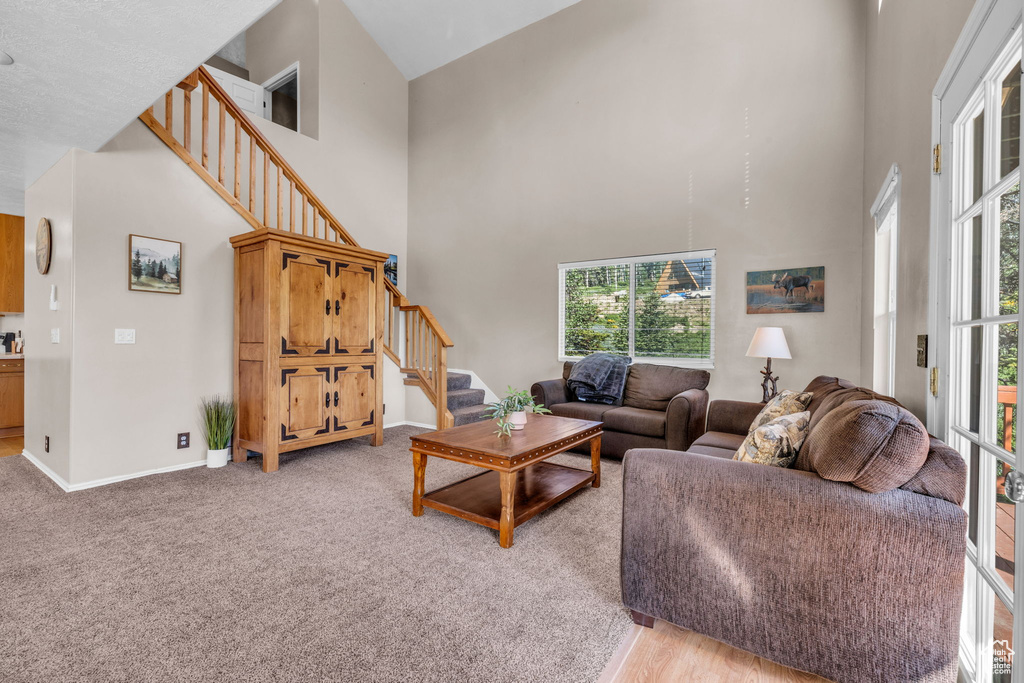 Living room with stairway, a towering ceiling, healthy amount of natural light, baseboards, and light colored carpet