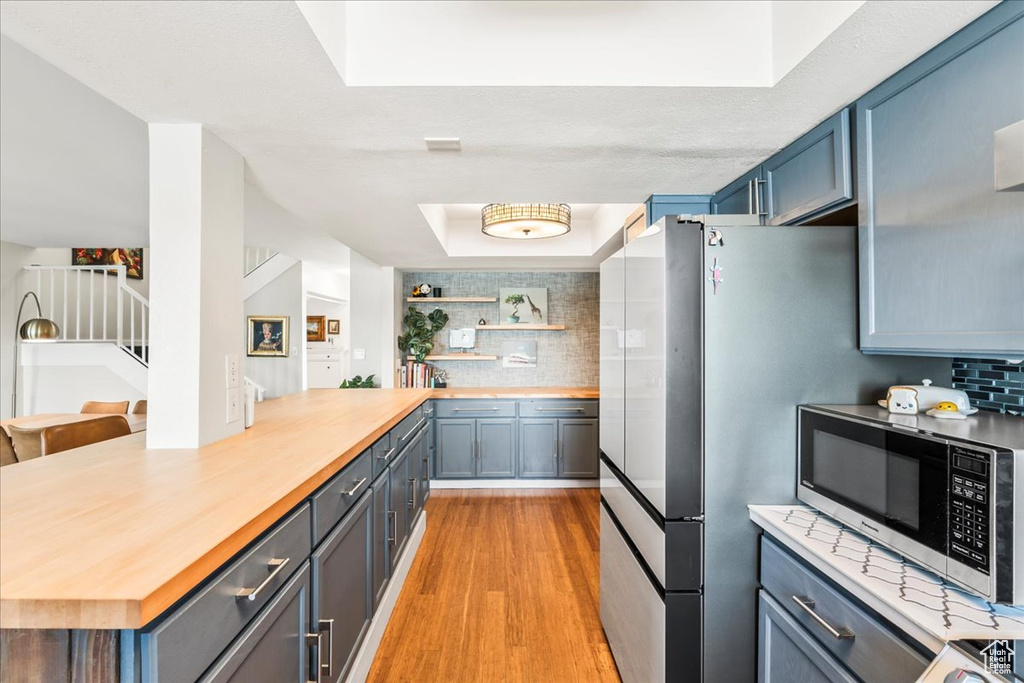 Kitchen featuring stainless steel appliances, wooden counters, light wood-style flooring, and backsplash
