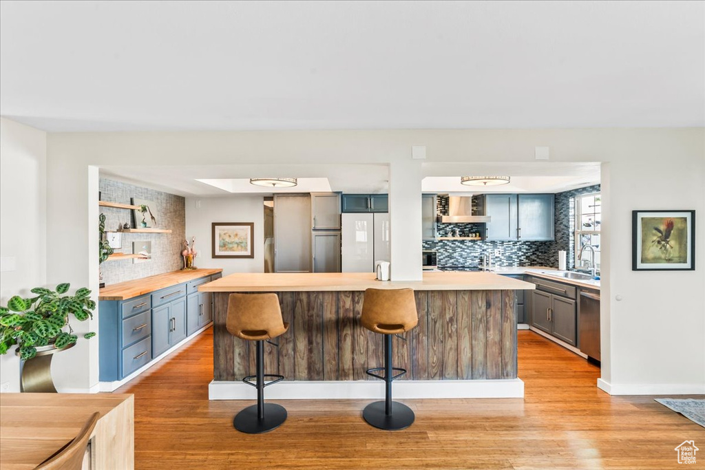 Kitchen with a kitchen breakfast bar, light wood-style flooring, wooden counters, stainless steel dishwasher, and a sink