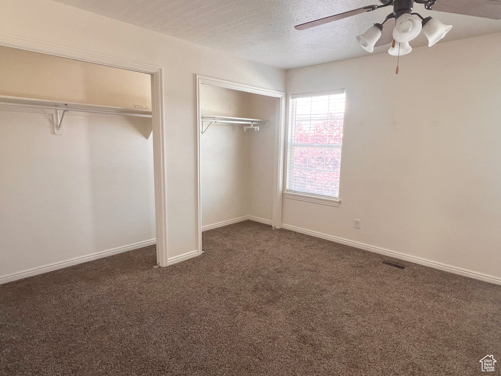 Unfurnished bedroom featuring two closets, dark colored carpet, a textured ceiling, a ceiling fan, and baseboards