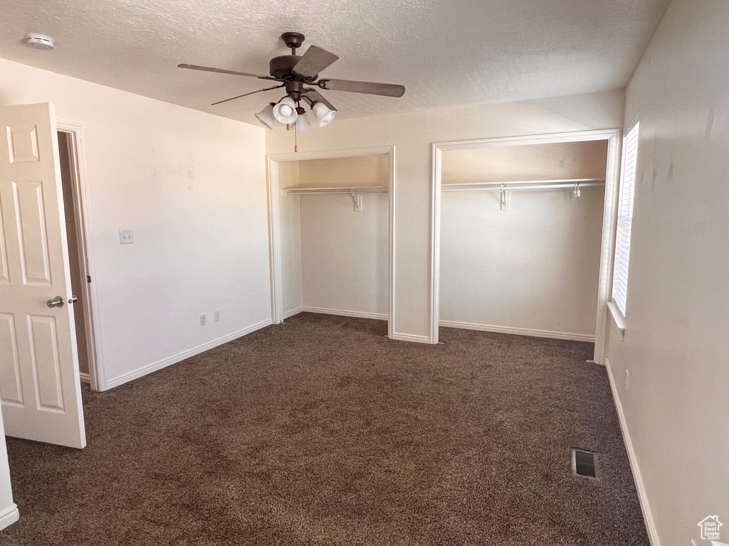 Unfurnished bedroom with multiple closets, dark colored carpet, a textured ceiling, ceiling fan, and baseboards
