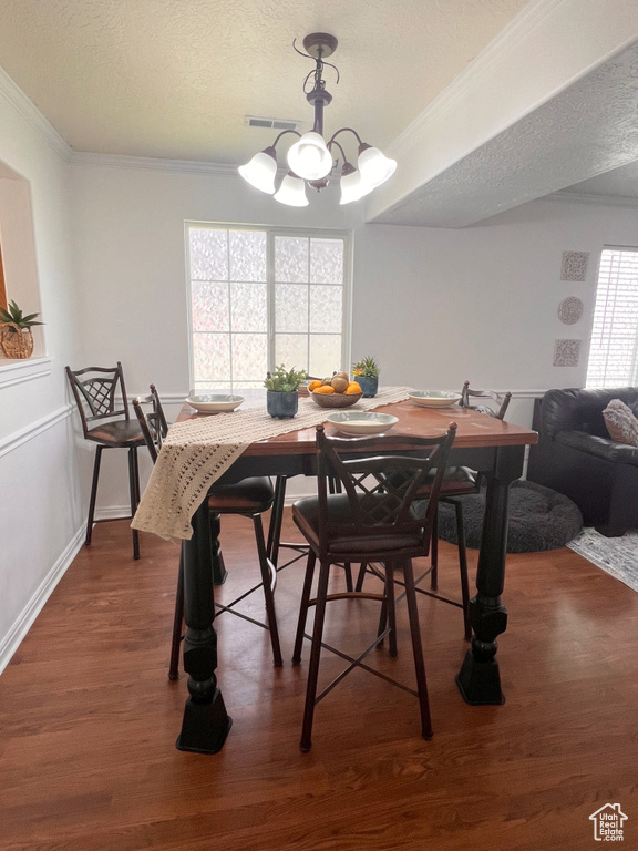 Dining room featuring a chandelier, ornamental molding, dark wood-style flooring, a textured ceiling, and baseboards