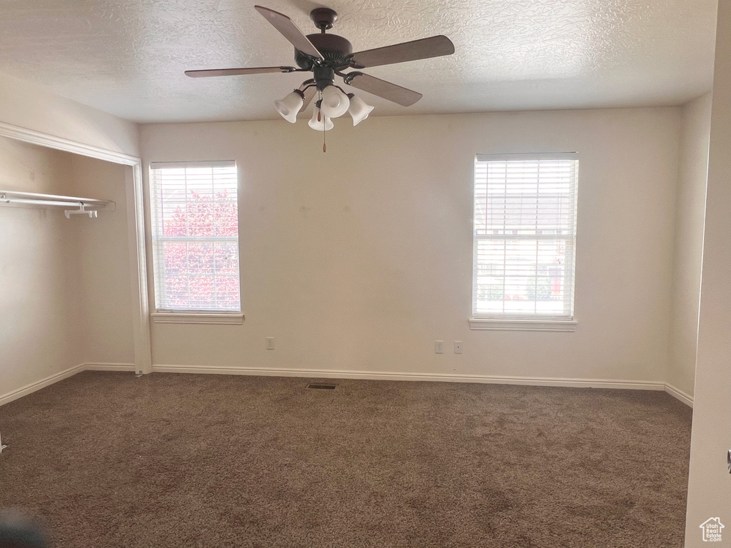 Unfurnished bedroom featuring a textured ceiling, dark carpet, multiple windows, and a closet