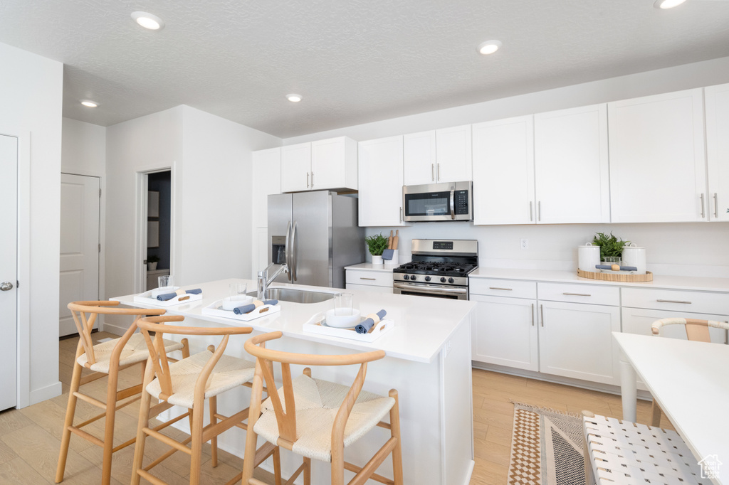 Kitchen with appliances with stainless steel finishes, a sink, white cabinetry, an island with sink, and recessed lighting