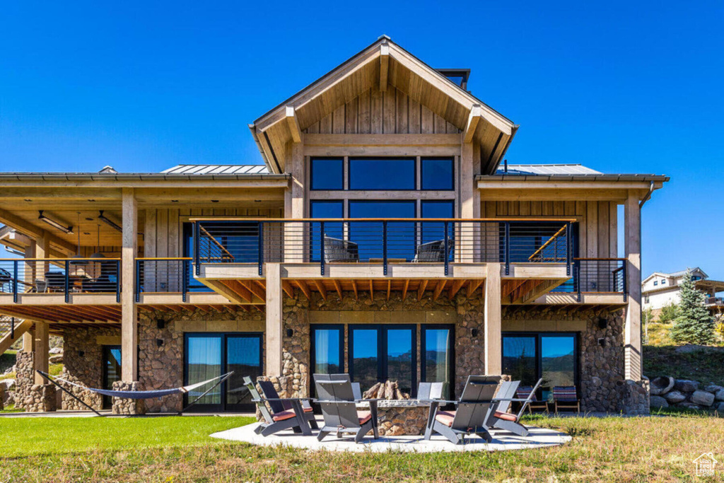 Rear view of property with a balcony, stone siding, a standing seam roof, a patio area, and board and batten siding