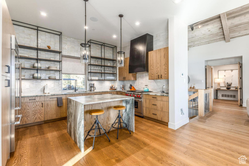 Kitchen featuring high quality appliances, range hood, open shelves, light wood-style flooring, and tasteful backsplash
