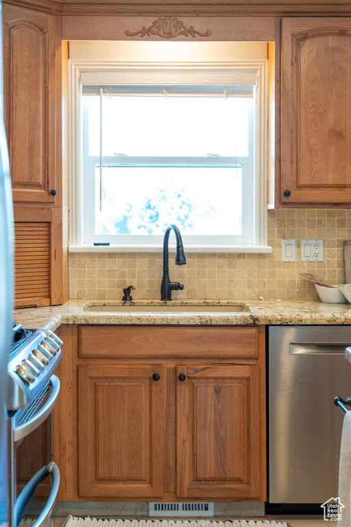 Kitchen with appliances with stainless steel finishes, a sink, backsplash, light stone counters, and brown cabinets