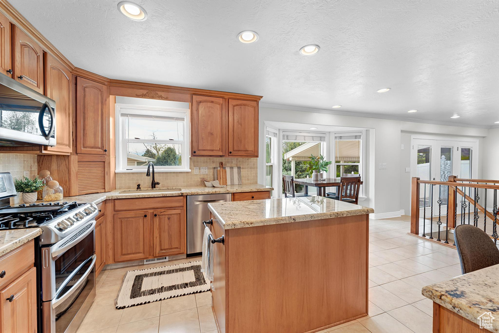Kitchen with stainless steel appliances, a sink, a center island, light tile patterned floors, and backsplash