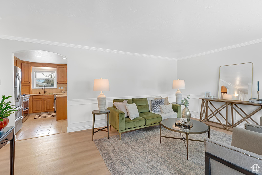 Living area featuring crown molding, light wood-style flooring, arched walkways, and wainscoting