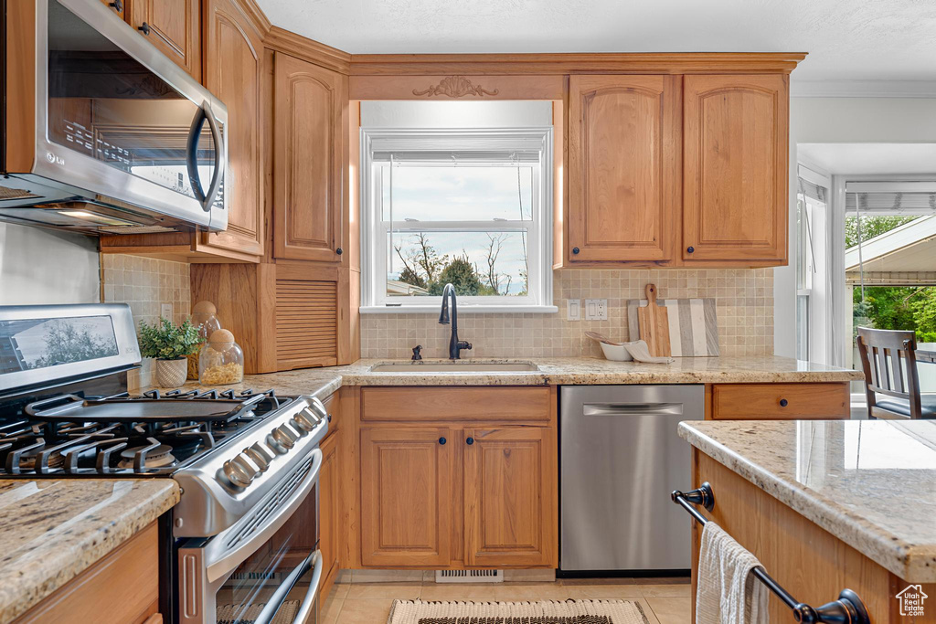 Kitchen with stainless steel appliances, a sink, tasteful backsplash, light stone countertops, and crown molding