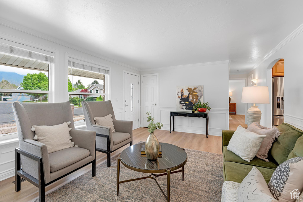 Living area featuring ornamental molding, arched walkways, and light wood-type flooring