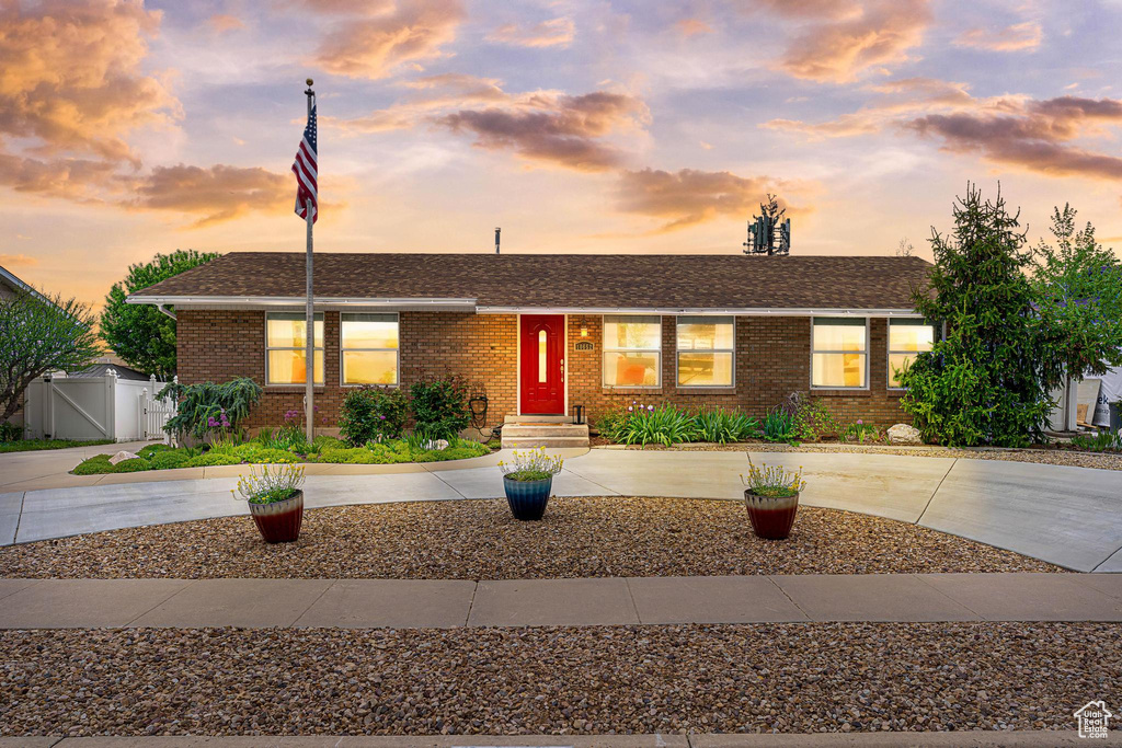 Single story home with curved driveway, brick siding, a gate, fence, and a shingled roof