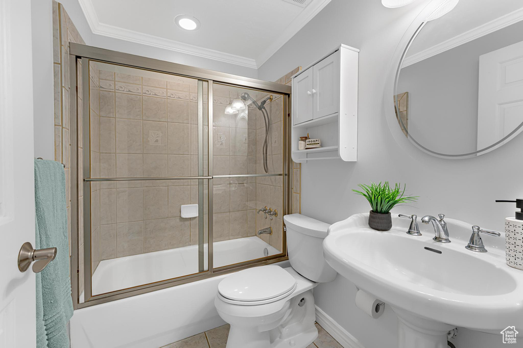 Bathroom featuring a sink, toilet, crown molding, combined bath / shower with glass door, and tile patterned flooring