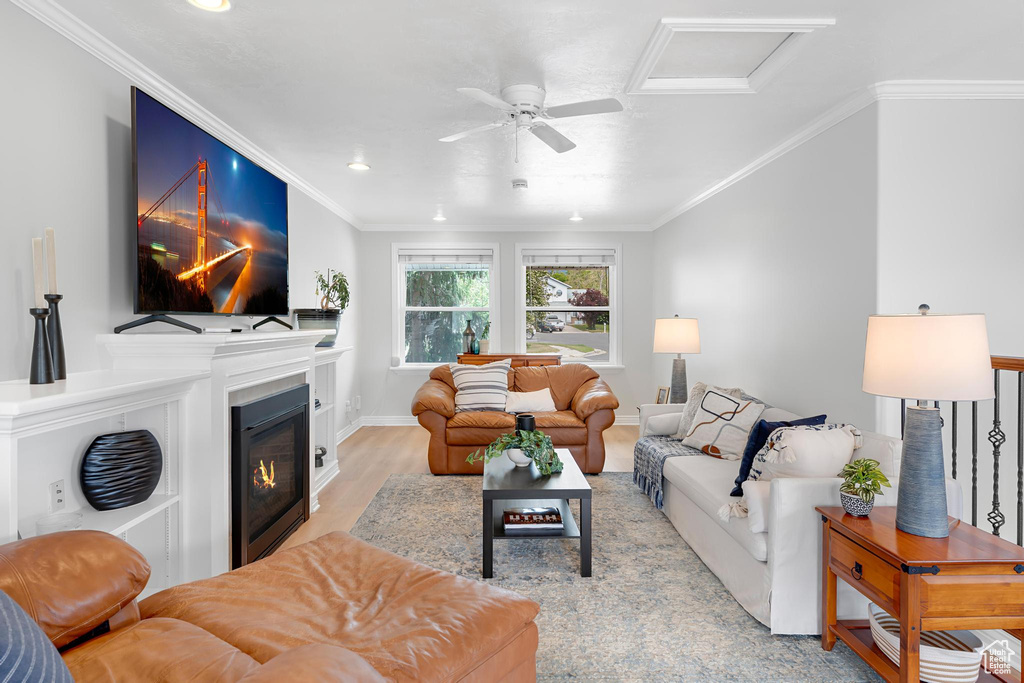 Living room featuring attic access, wood finished floors, ornamental molding, recessed lighting, and a glass covered fireplace
