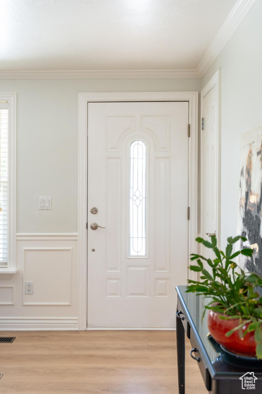 Foyer entrance with light wood-style flooring, crown molding, and wainscoting