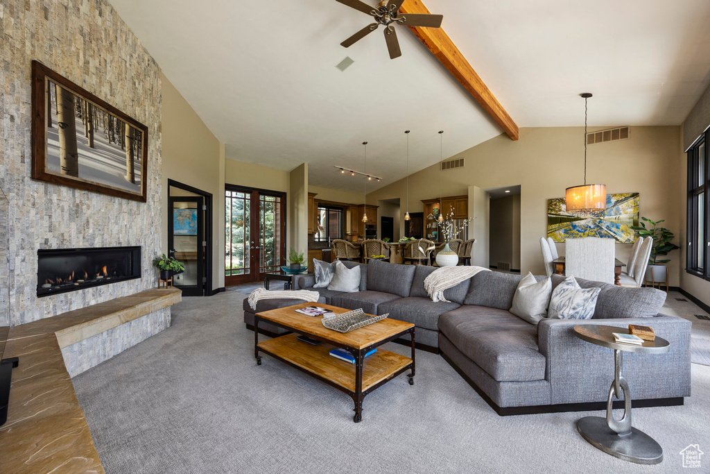 Living room featuring beamed ceiling, a stone fireplace, a ceiling fan, high vaulted ceiling, and carpet flooring