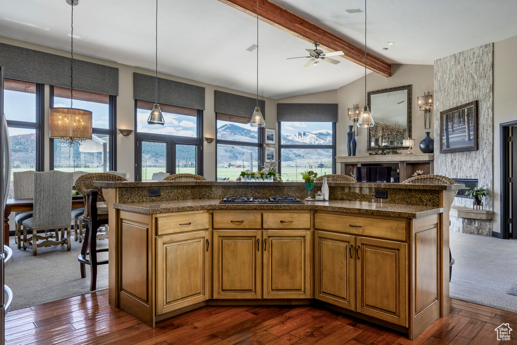 Kitchen with a fireplace, gas stovetop, a ceiling fan, decorative light fixtures, and brown cabinets
