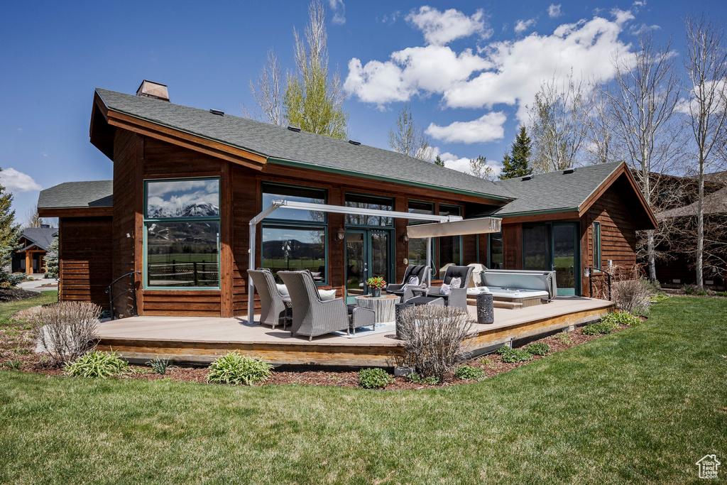 Rear view of house featuring a wooden deck, a yard, an outdoor hangout area, and roof with shingles