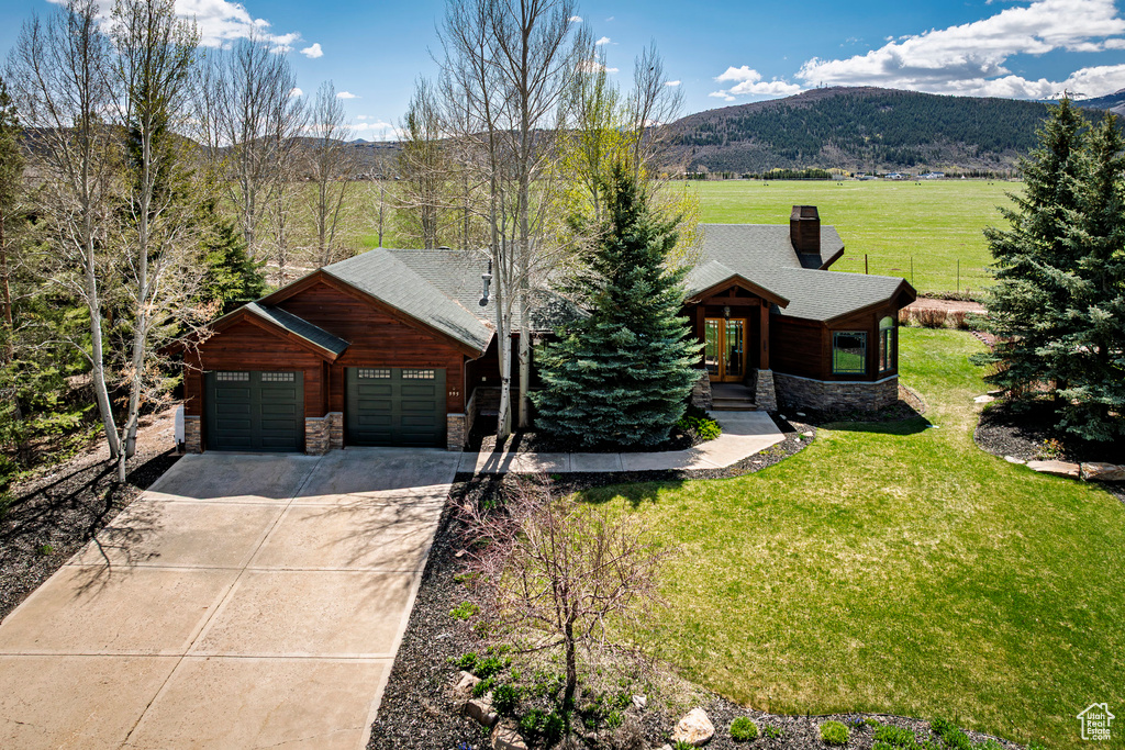 View of front facade with stone siding, a mountain view, concrete driveway, a front yard, and a garage