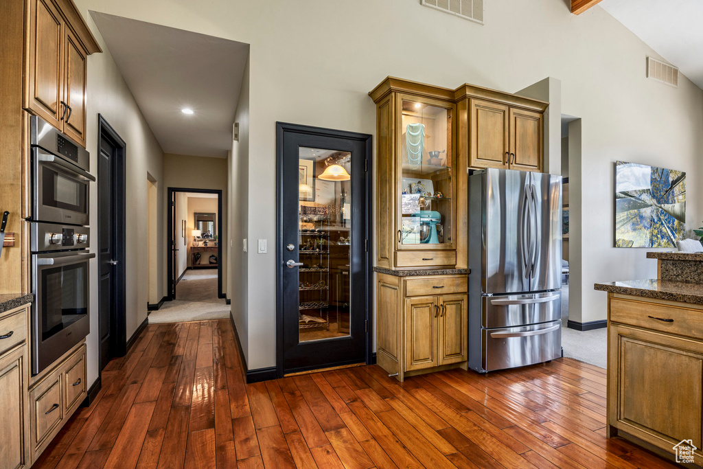 Kitchen featuring stainless steel appliances, dark wood-style flooring, baseboards, dark stone counters, and high vaulted ceiling