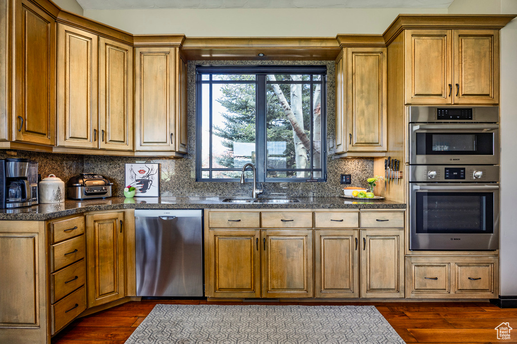 Kitchen with stainless steel appliances, a sink, dark wood-type flooring, backsplash, and dark countertops