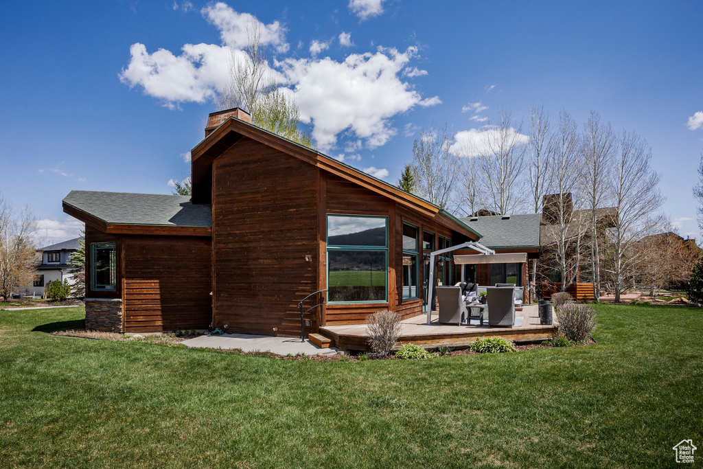 Rear view of property with a chimney, a wooden deck, a lawn, a sunroom, and roof with shingles