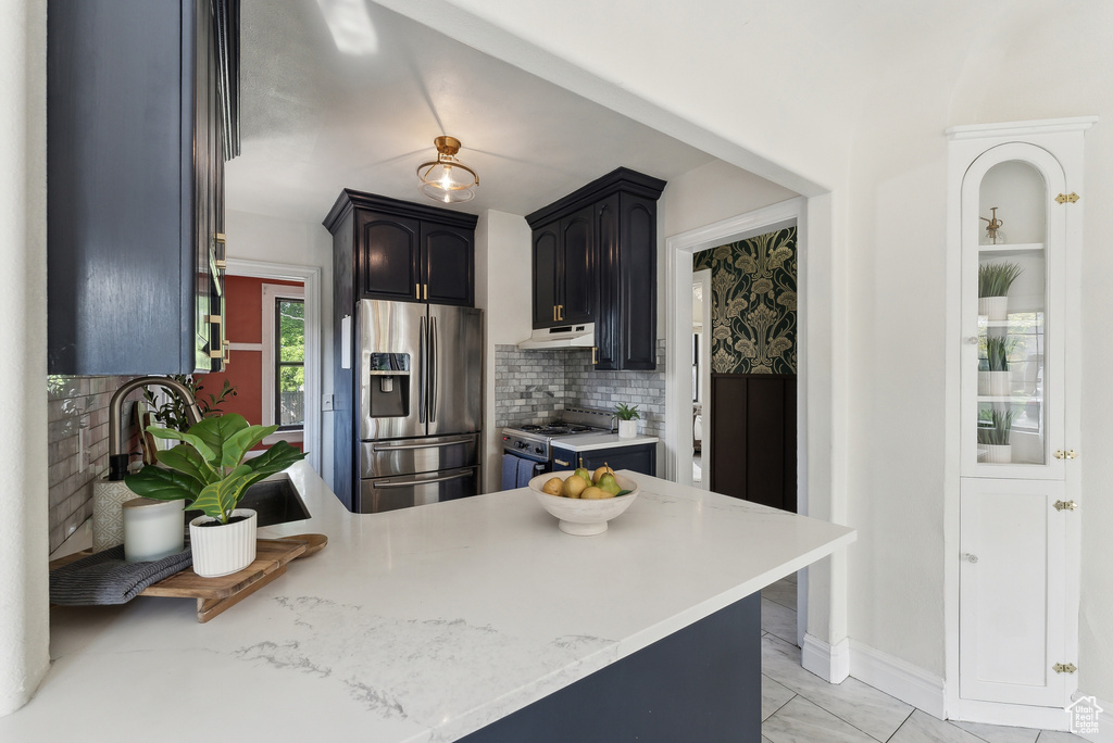 Kitchen featuring a sink, a peninsula, decorative backsplash, stainless steel fridge, and range with gas stovetop